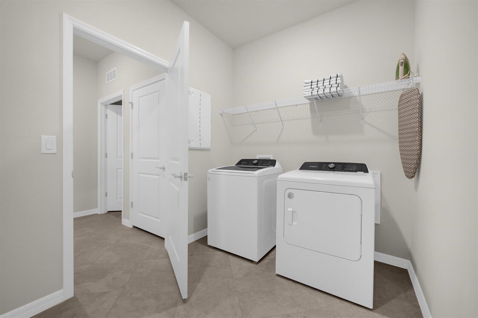 A laundry room with two white washing machines, a drying rack, and a shelf with folded towels.