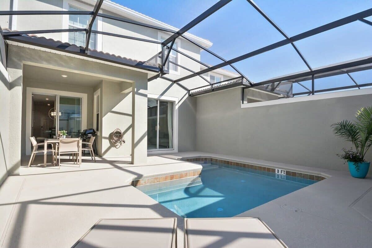 A swimming pool with a glass ceiling, a patio area with a table and chairs, and a potted plant.