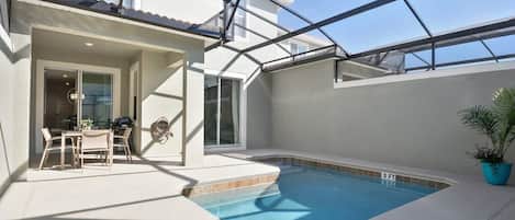 A swimming pool with a glass ceiling, a patio area with a table and chairs, and a potted plant.