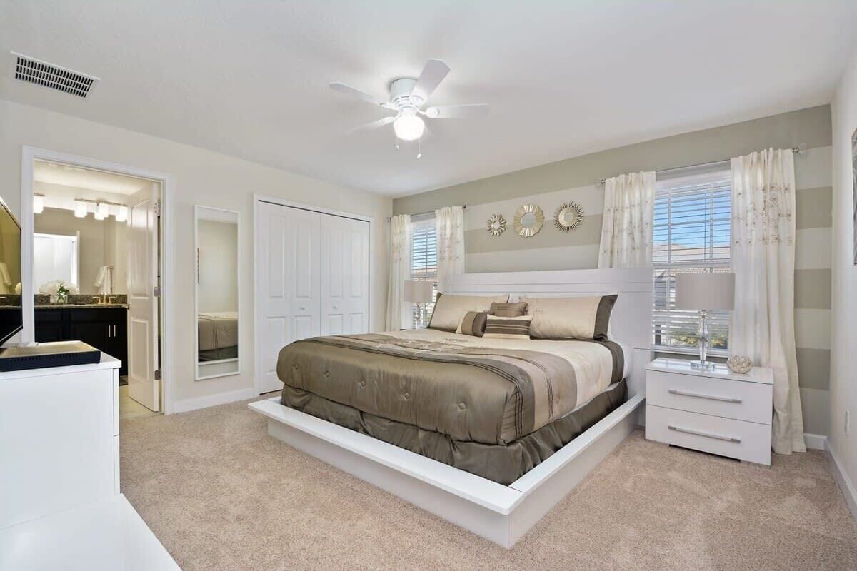 A bedroom with a bed, a nightstand, a ceiling fan, and a window with curtains.