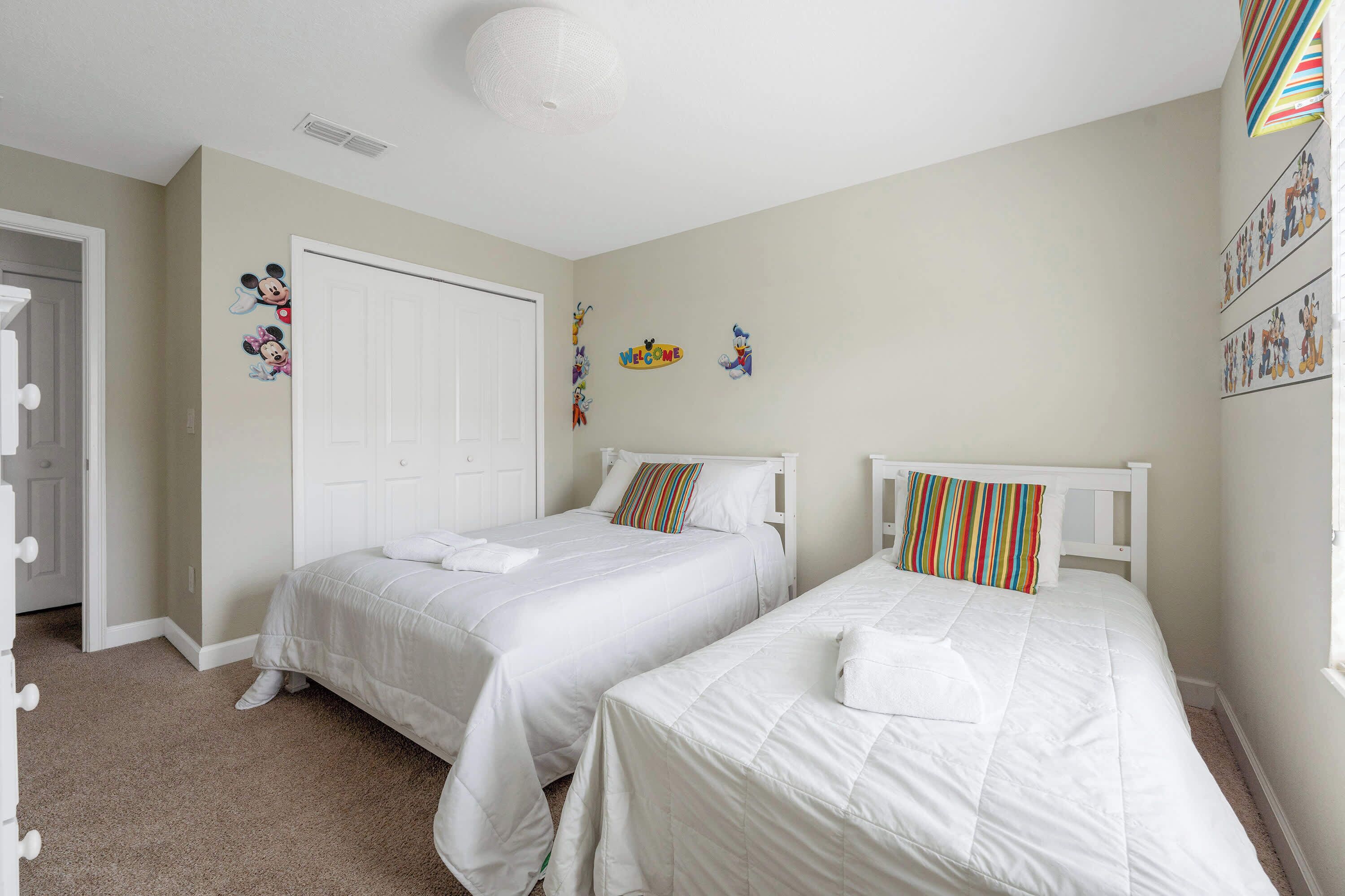 A bedroom with two beds, a white door, and wall decorations including cartoon characters.