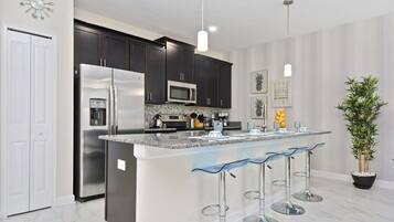 A modern kitchen with dark cabinets, stainless steel appliances, a marble countertop, and a central island with bar stools.