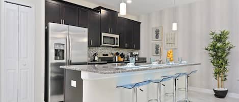 A modern kitchen with dark cabinets, stainless steel appliances, a marble countertop, and a central island with bar stools.