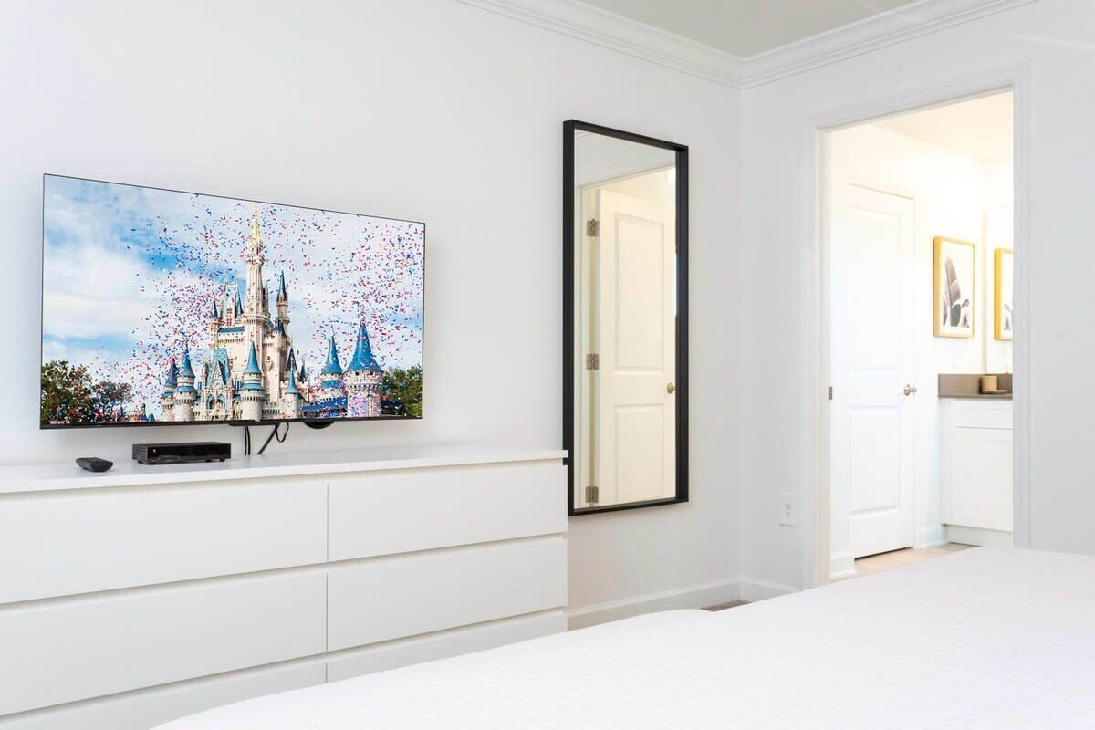 Quarto com televisão de tela plana grande fixada na parede, uma cama, uma porta e um pequeno armário.