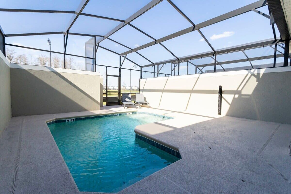A swimming pool with a glass enclosure, lounge chairs, and a clear view of the sky.