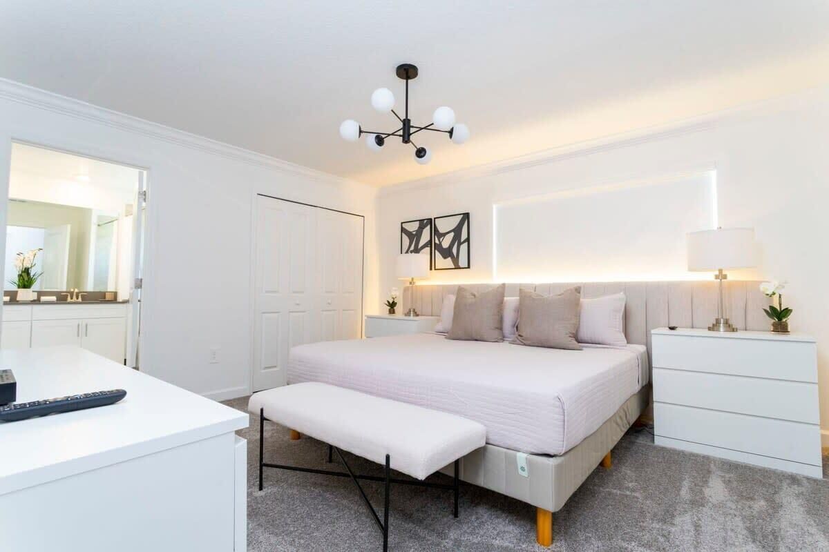 A bedroom with a bed, bedside tables, a desk, a bench, a mirror, and a ceiling light fixture.