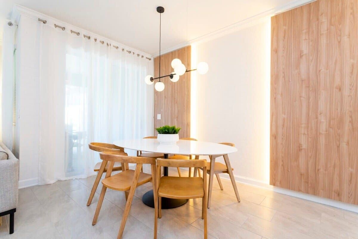 Et moderne spiseområde med et rundt bord, træstole, en hængende lampe og en trævæg.