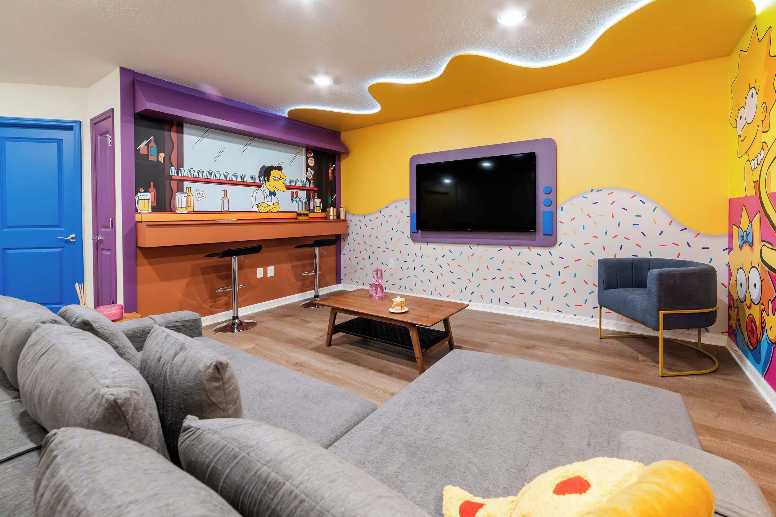 Sala de estar con sofá, una mesa de centro, televisor y una zona de bar con un caricaturista.