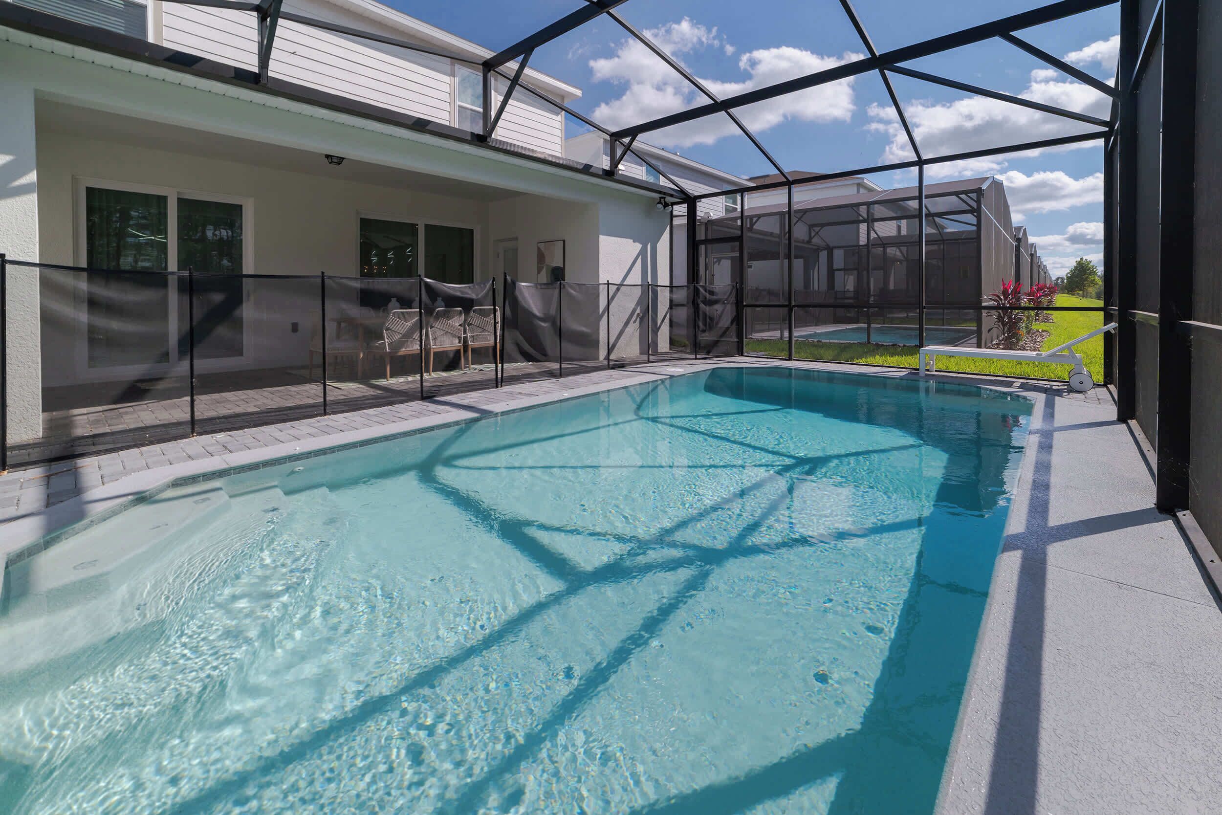 A swimming pool with a covered area, a clear sky, and a view of a house.