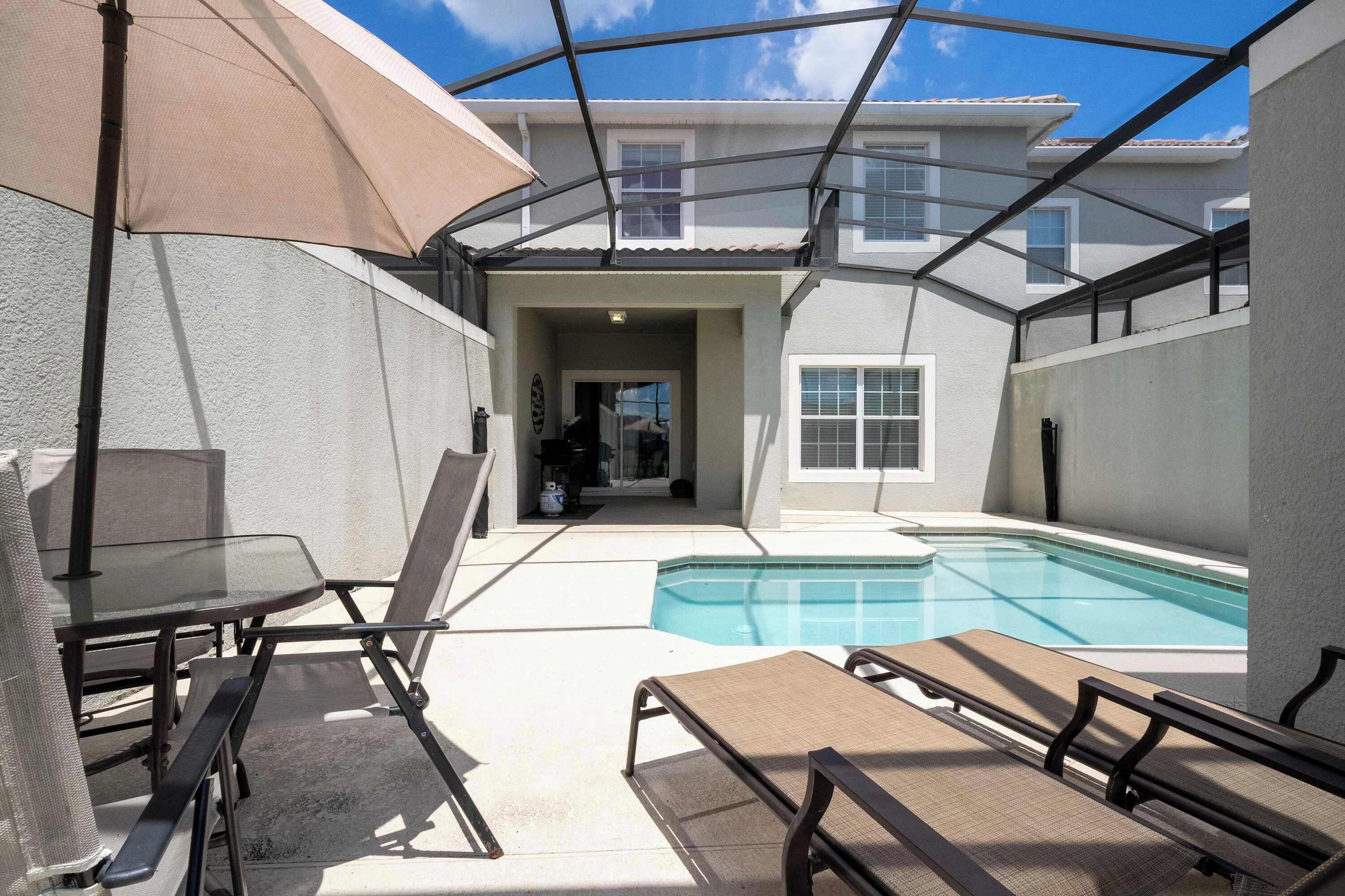 A covered outdoor area with a pool, lounge chairs, and a table with chairs.