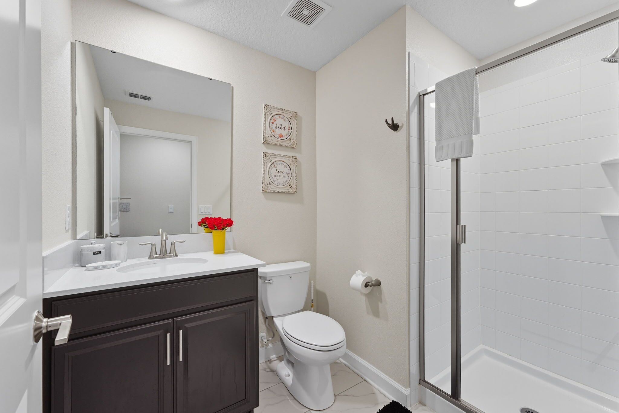 A modern bathroom with a white sink, dark cabinets, a toilet, and a glass-enclosed shower.