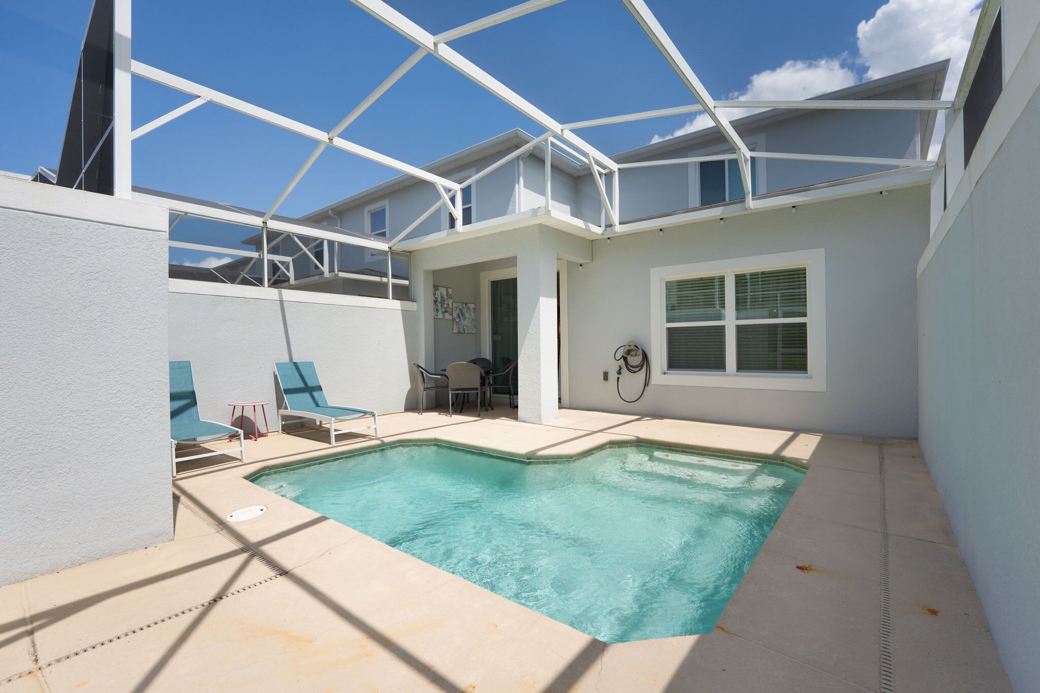 Una piscina con sillas de descanso, un porche cubierto y una pared exterior blanca.