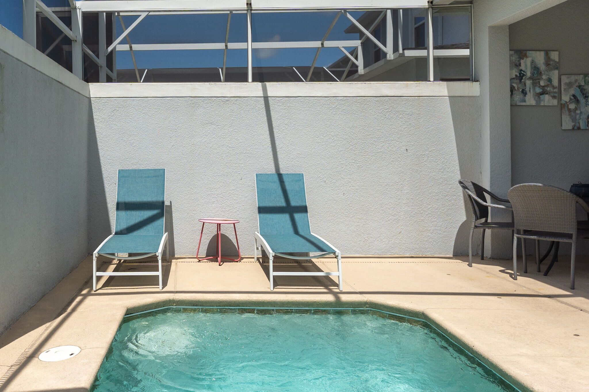 A pool area with two lounge chairs and a table, a small stool, and a chair.
