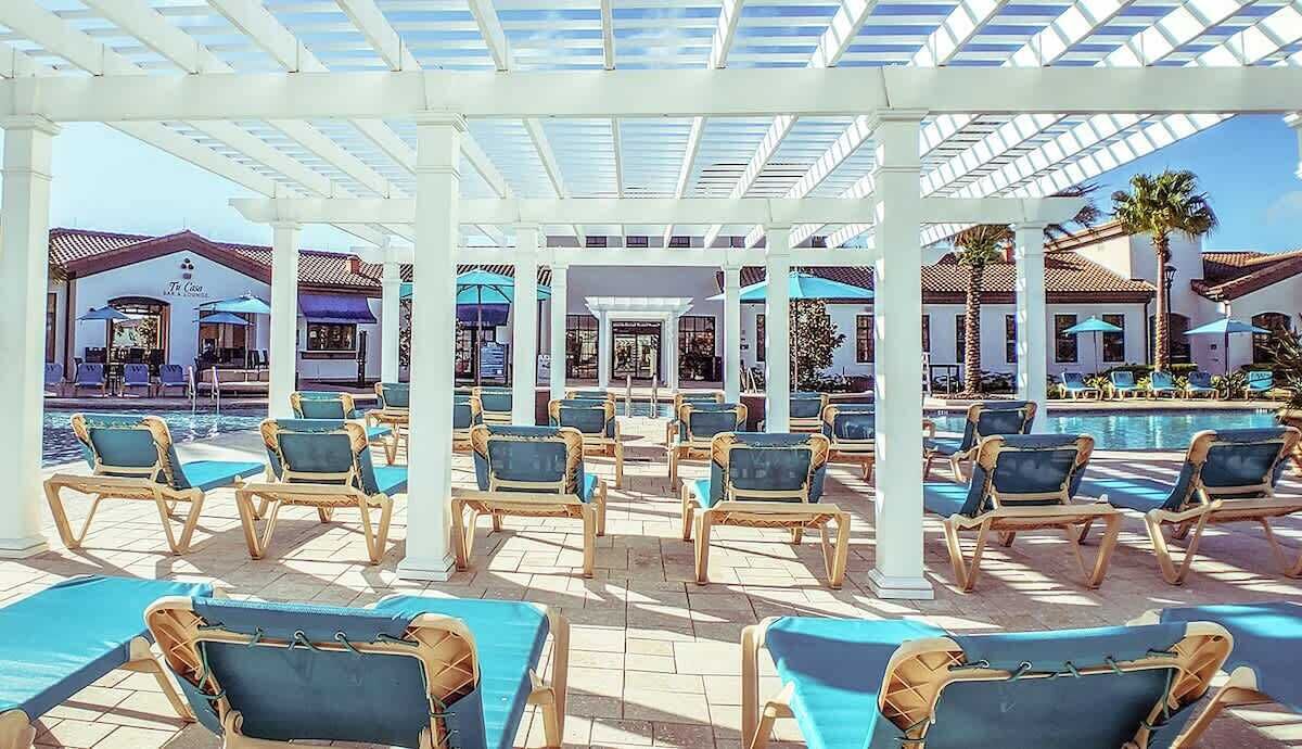 A covered pool area with lounge chairs and umbrellas, a bar, and a building with a sign that reads "The Cove".