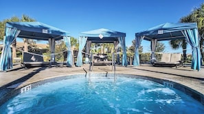 Ein Swimmingpool mit Whirlpool, zwei überdachten Sitzbereichen und einem strahlend blauen Himmel.
