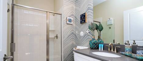A bathroom with a glass shower enclosure, a white toilet, a marble-patterned wall, a sink with a mirror, and decorative items.