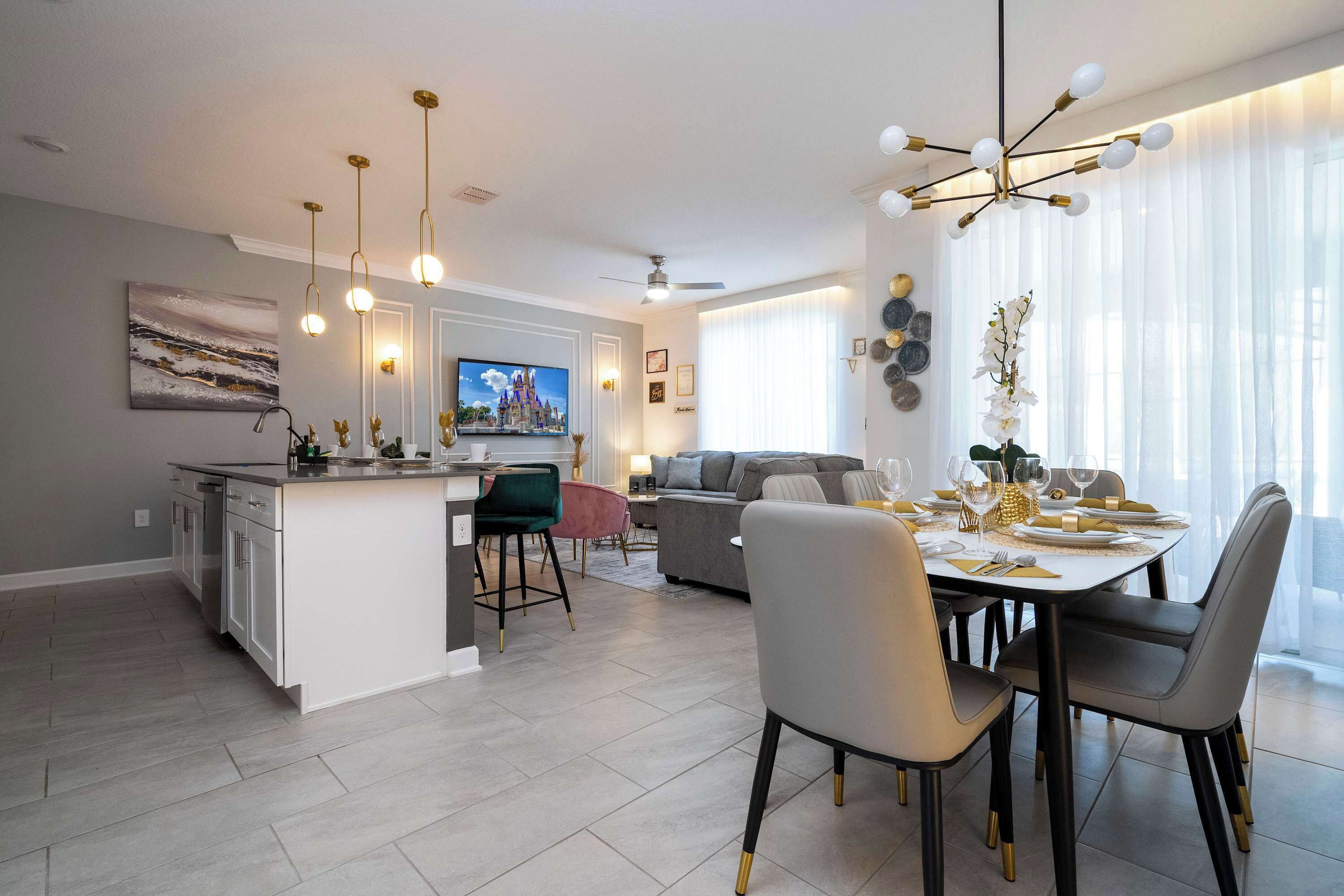 Una cucina moderna con isola centrale, zona pranzo con tavolo rotondo e soggiorno con divano e televisore.