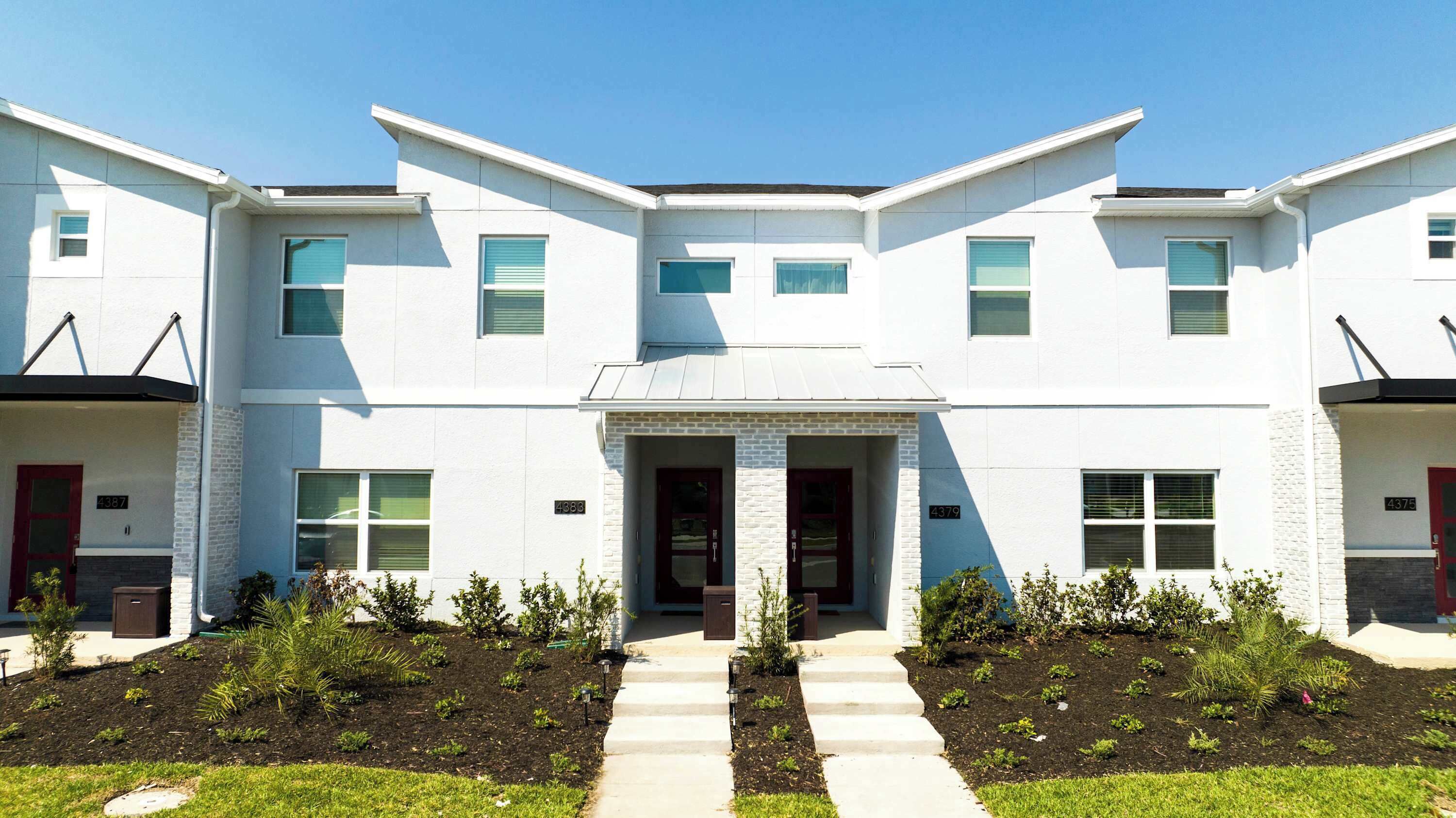 A modern two-story building with a symmetrical facade, a central entrance with double doors, and a small porch area.