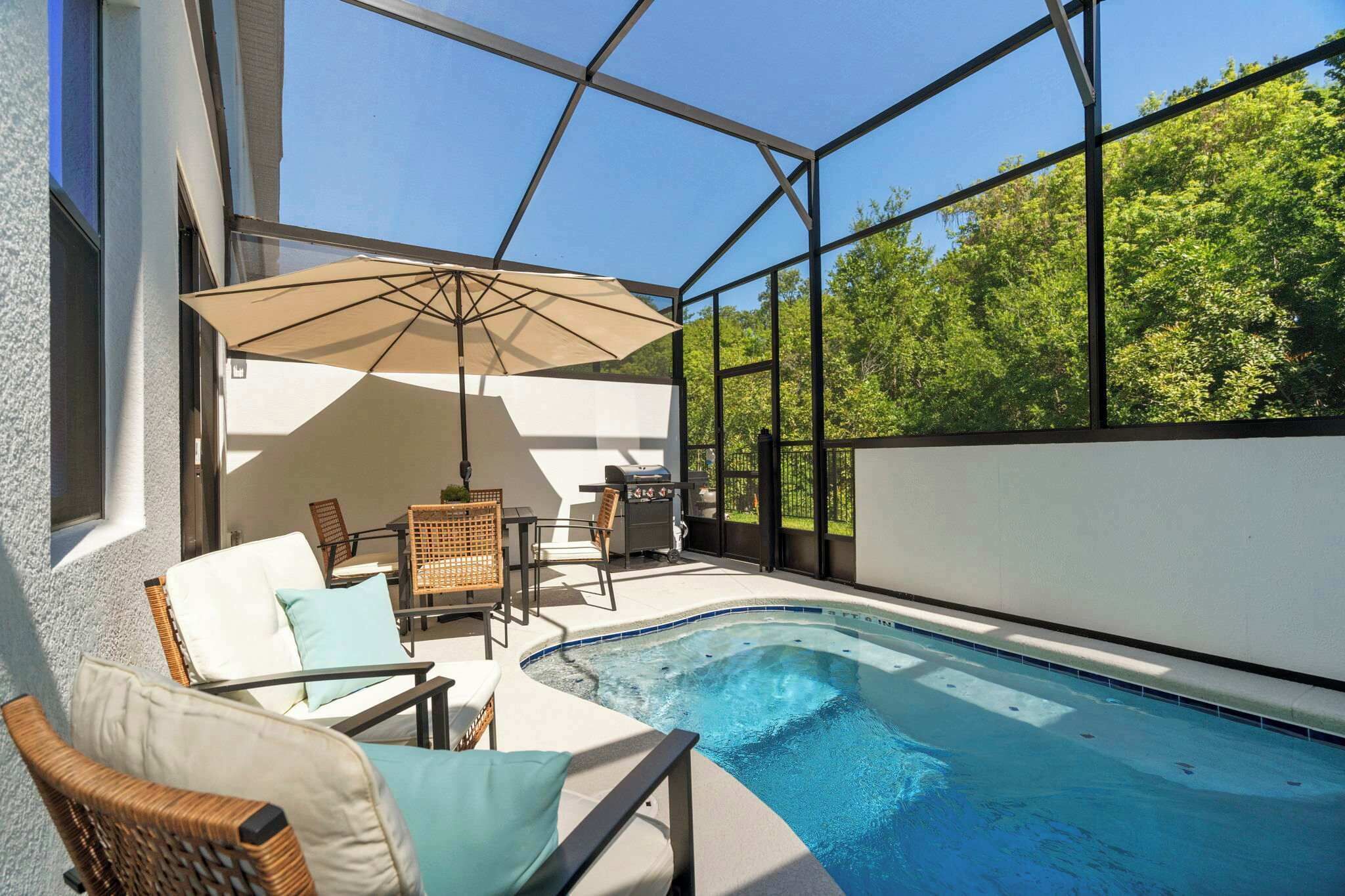 An indoor swimming pool with a glass enclosure, lounge chairs, a table, and an umbrella.