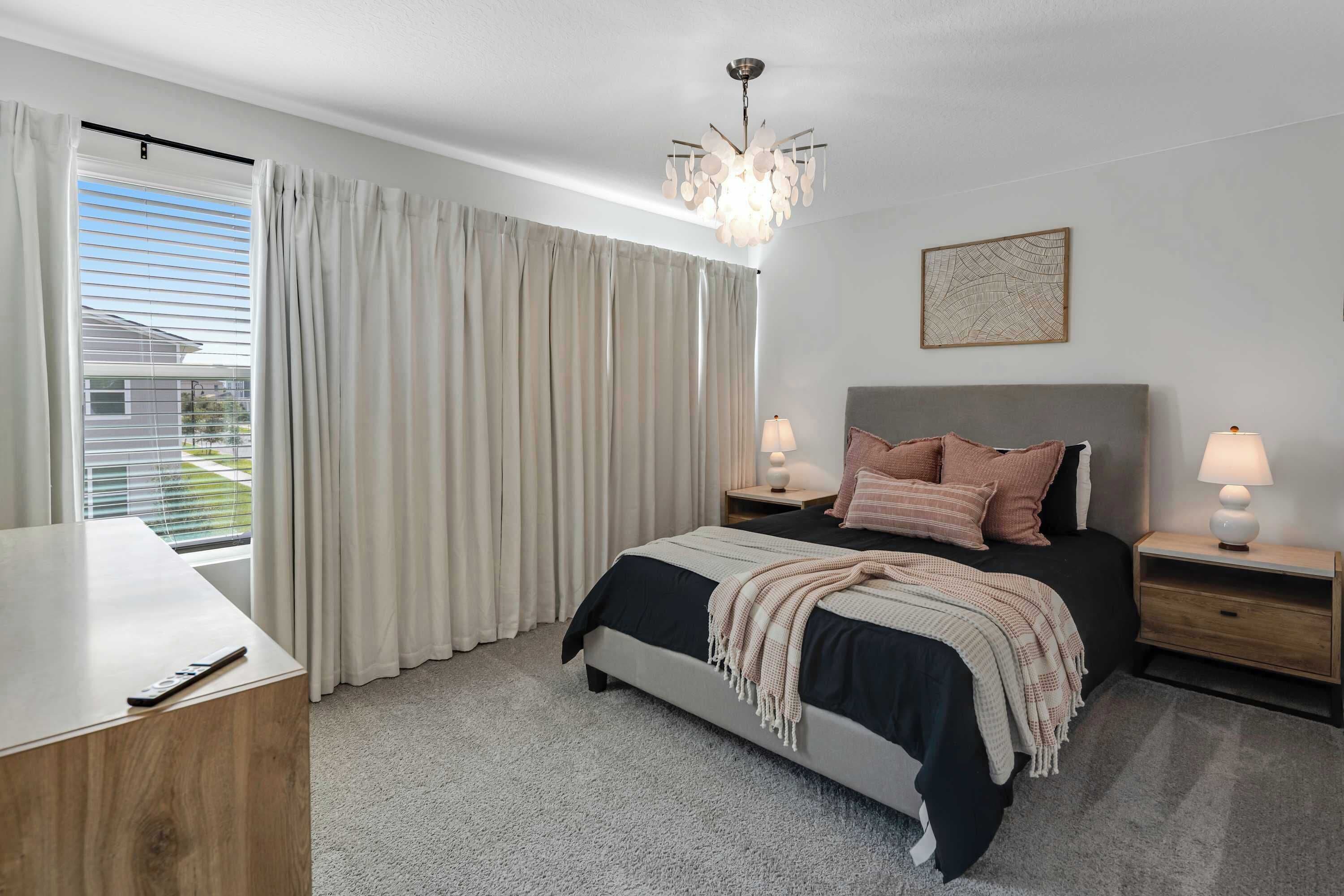 A bedroom with a bed, bedside tables, a chandelier, and a window with curtains.