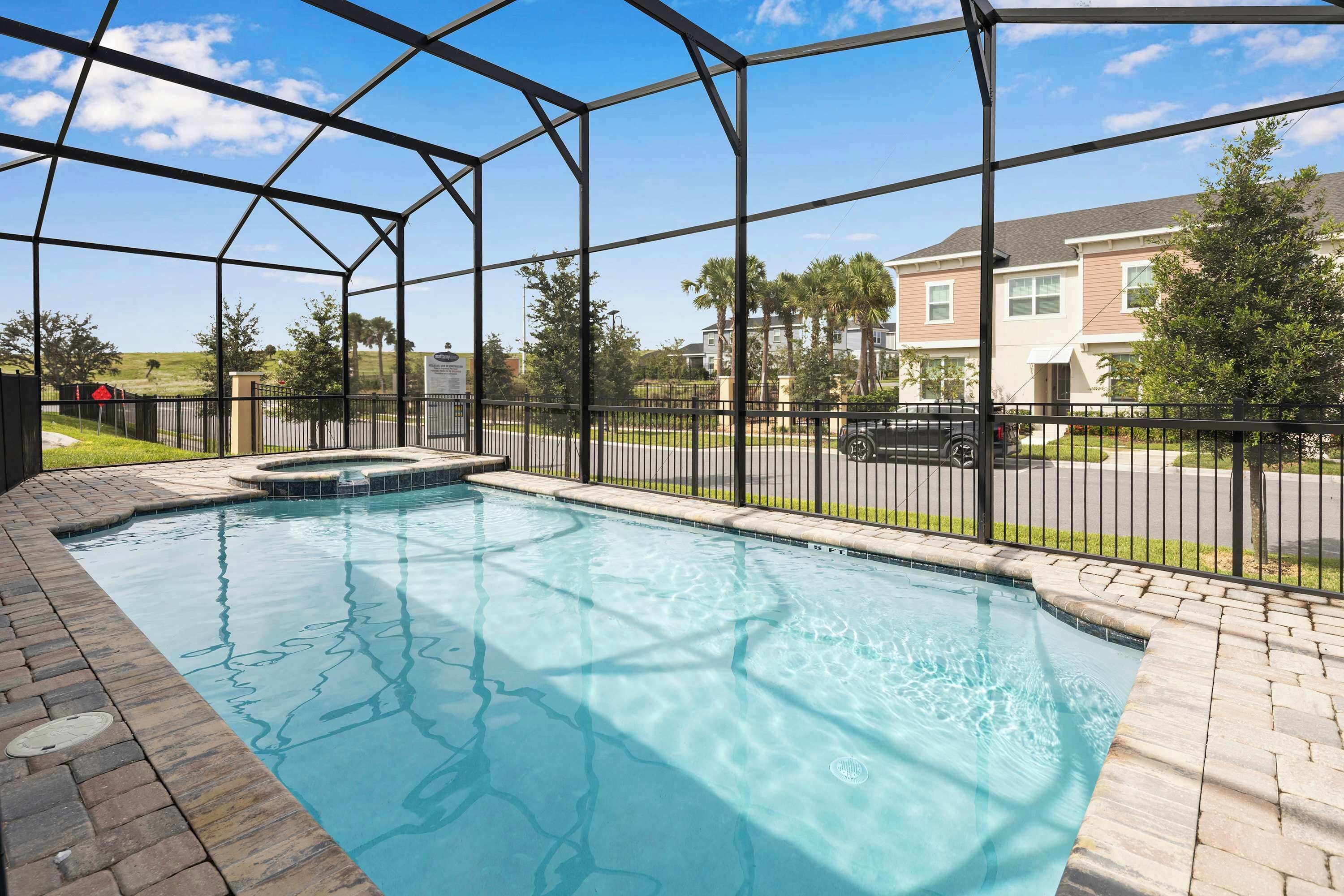 A swimming pool with a hot tub, surrounded by a metal fence, and a view of residential buildings in the background.