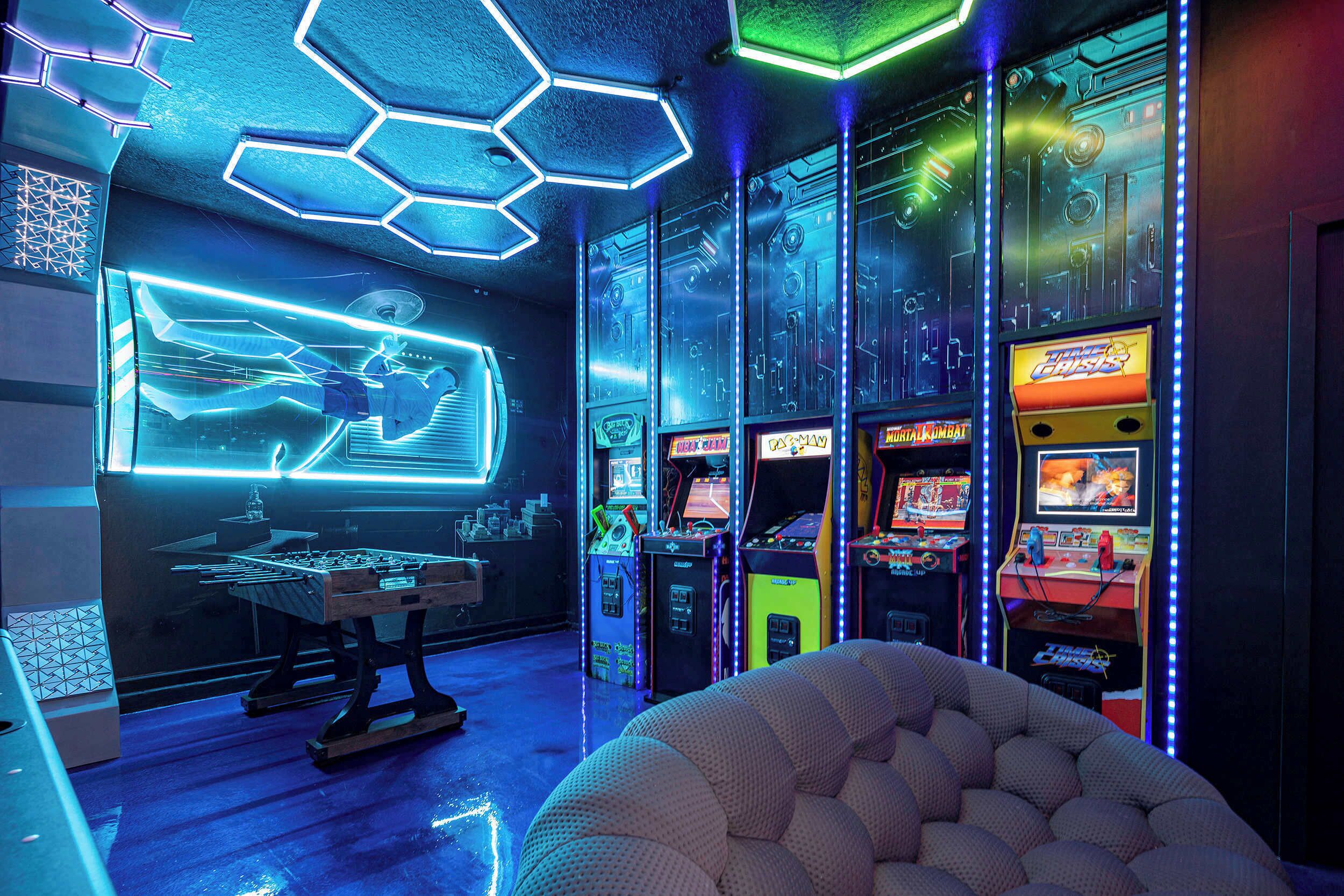 Una sala giochi con luci al neon, diverse macchine da gioco e una zona salotto confortevole.
