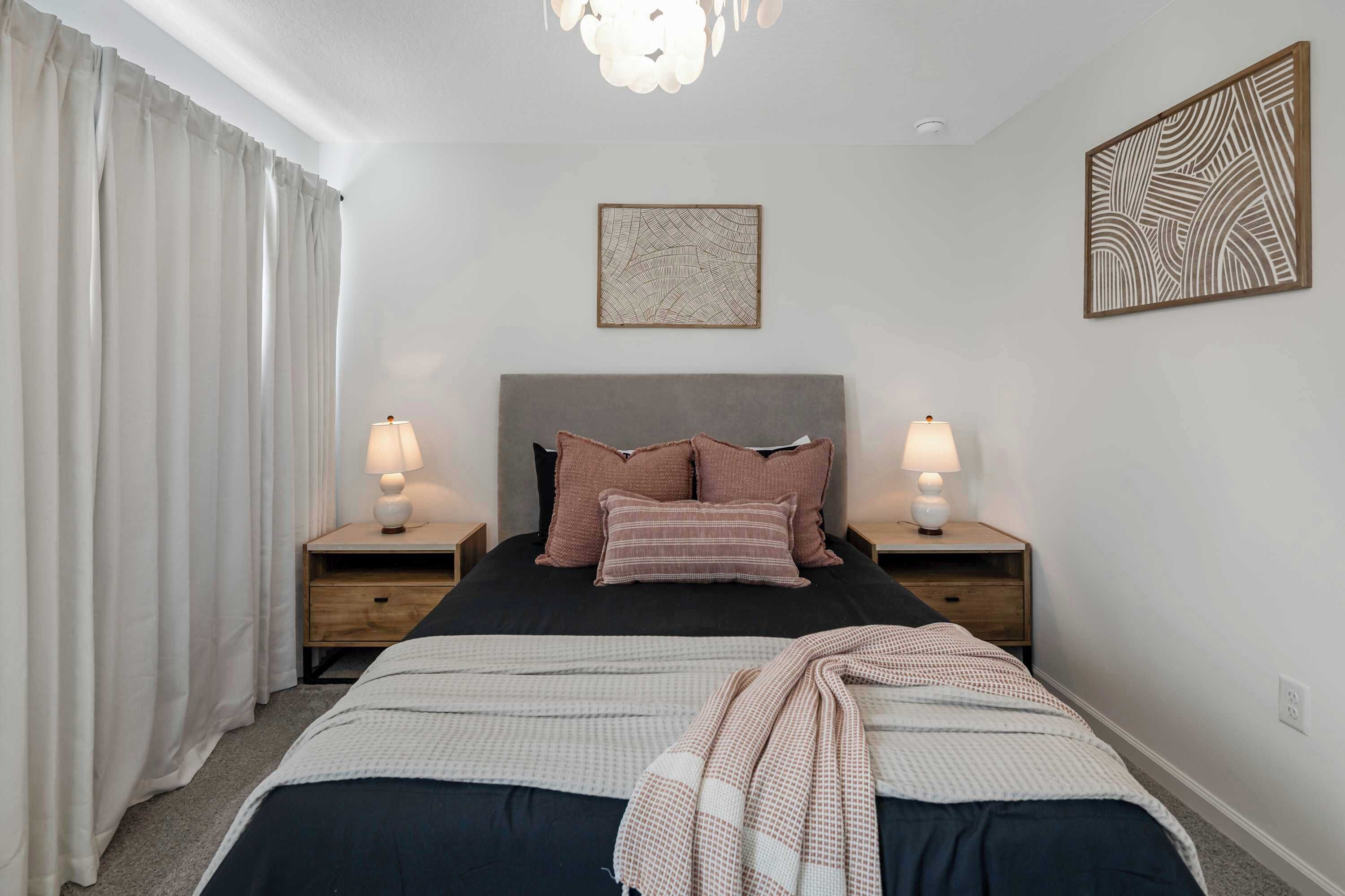 A neatly arranged bedroom with a large bed, two bedside tables with lamps, a headboard, and two wall art pieces.