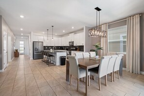 A modern kitchen with white cabinets, a central island, and a dining area with a wooden table and chairs. - Gorgeous 6-bedroom House With Private Pool (Davenport)