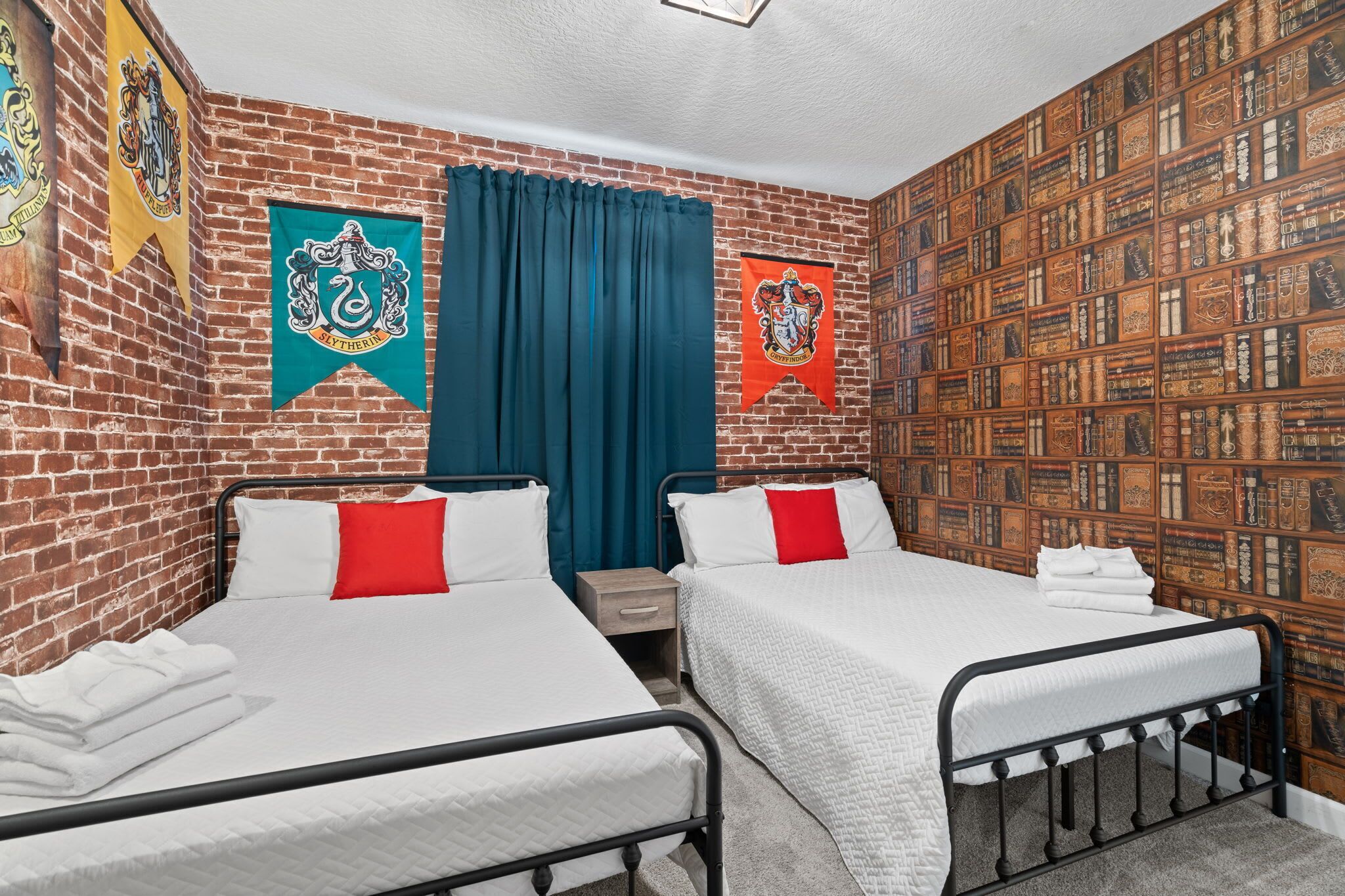 A room with two beds, a brick wall, and a bookshelf.