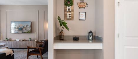 A living room with a sofa, a coffee table, a TV, a plant, and a shelf with a camera and a lantern.