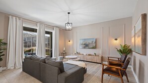 Ein modernes Wohnzimmer mit einer Eckcouch, einem Essbereich mit einem Holzhocker, einem runden Tisch und einem Gemälde an der Wand.