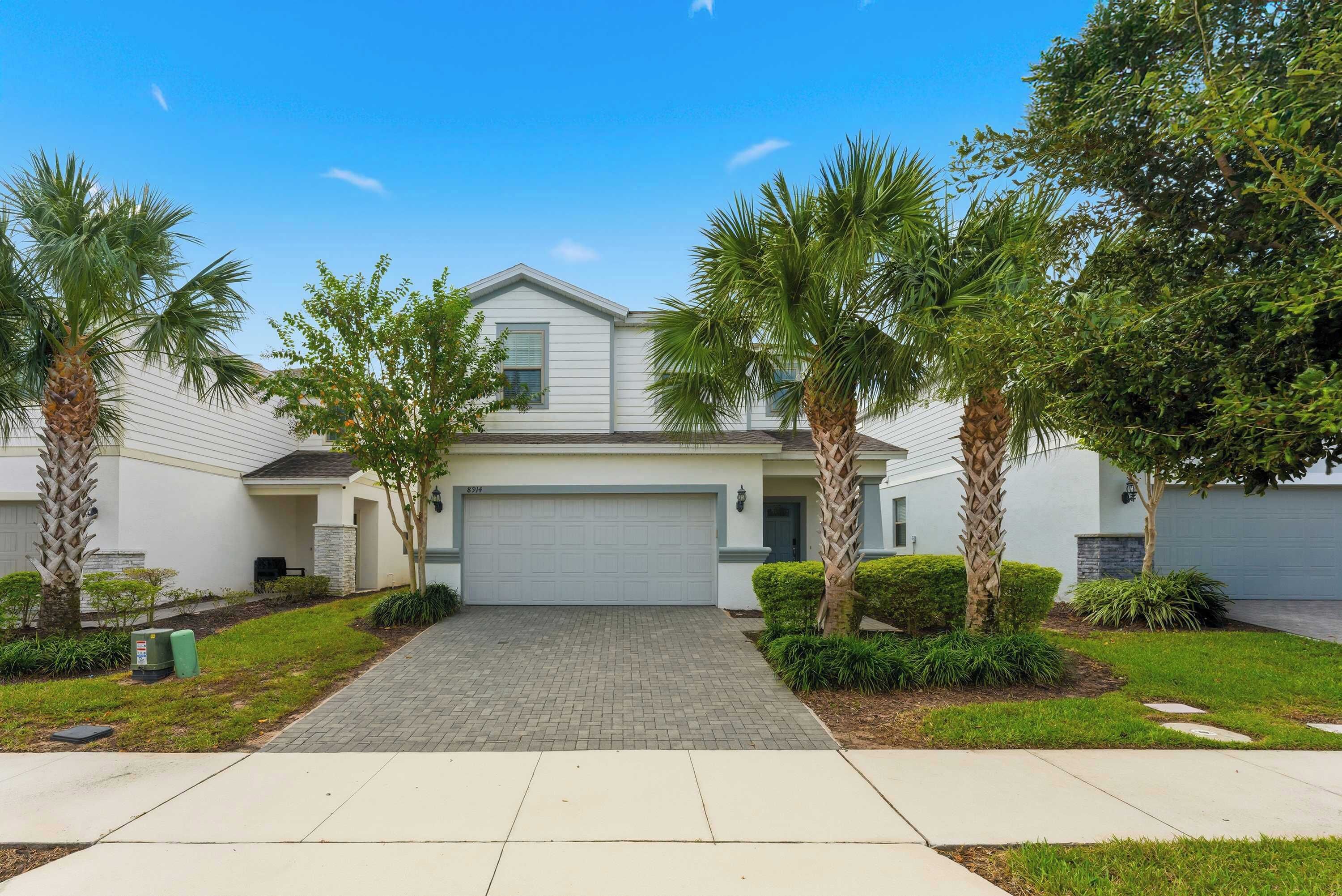 A residential house with a garage, a paved driveway, and palm trees.