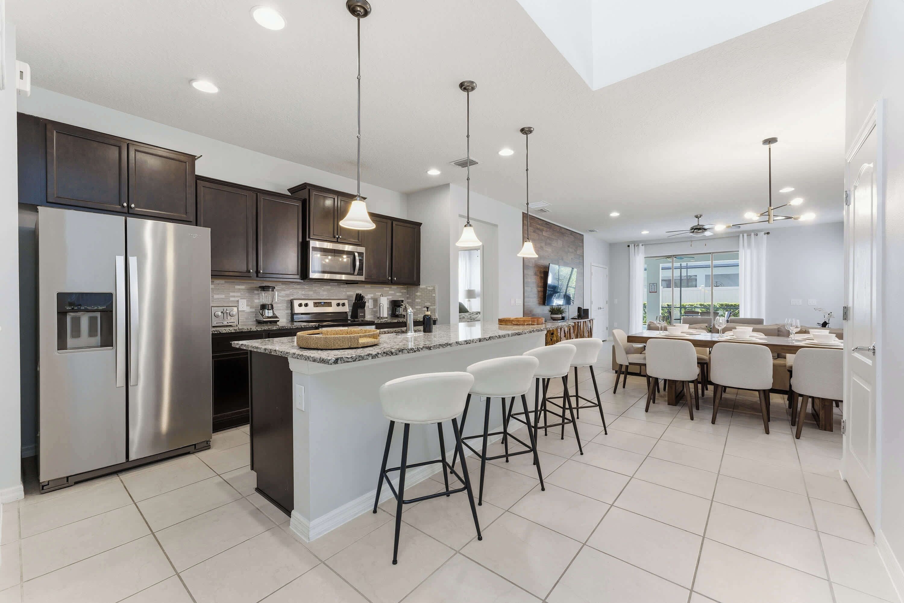 A modern kitchen with a stainless steel refrigerator, a microwave, and a large island with bar stools.