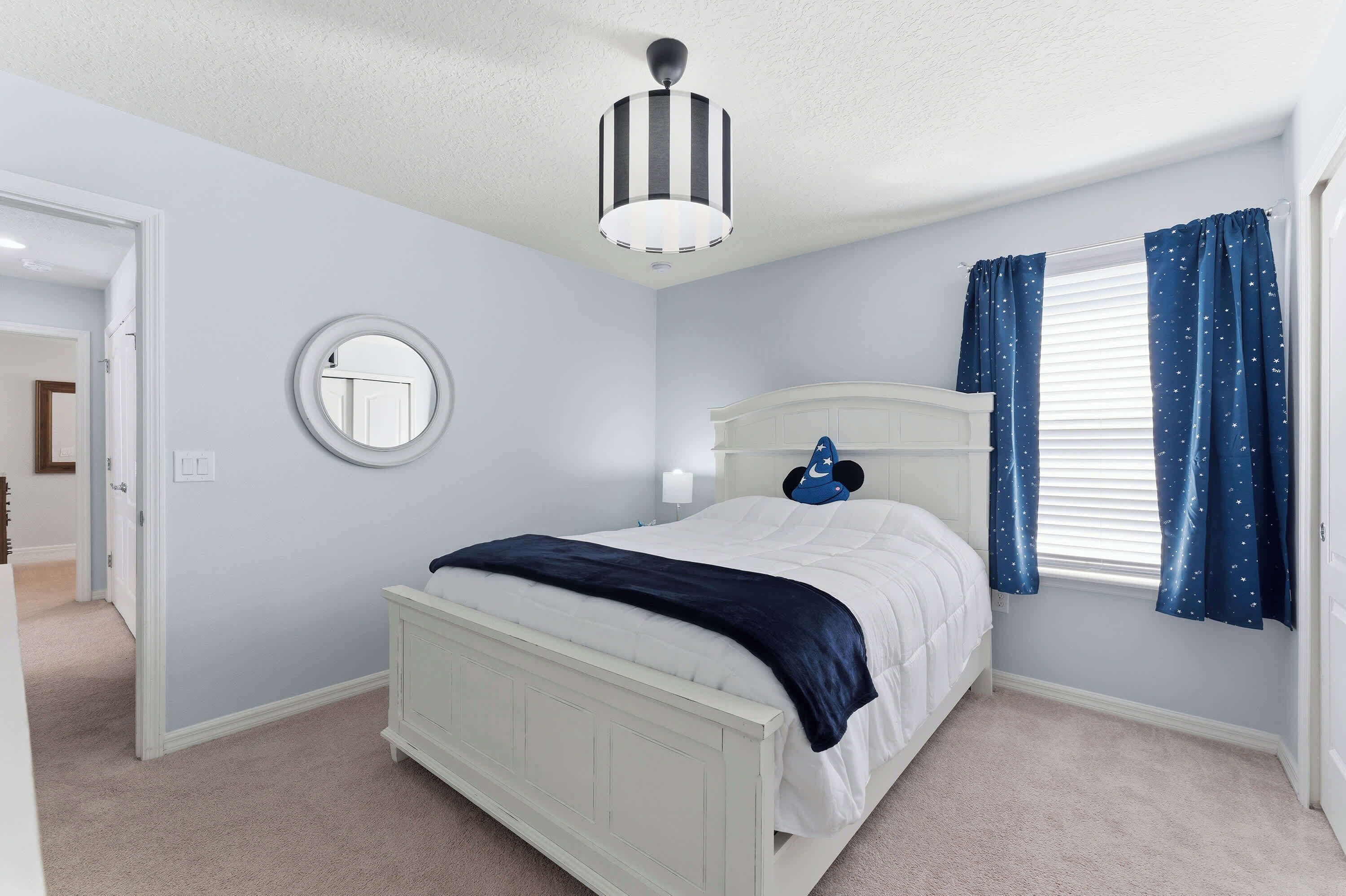 A bedroom with a bed, a round mirror, a ceiling light fixture, and a window with curtains.