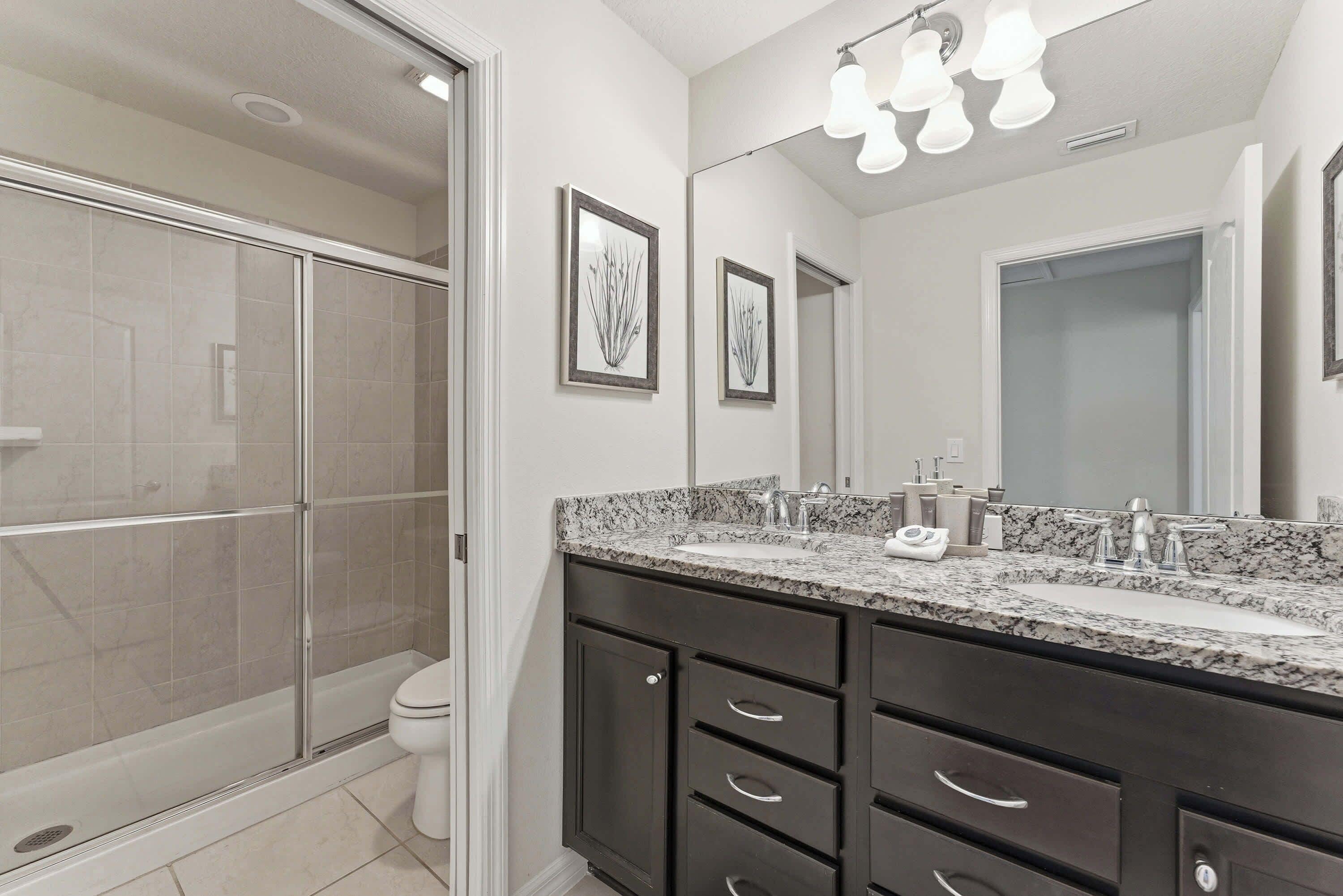 Une salle de bain moderne avec une douche à parois de verre, des meubles de rangement aux couleurs sombres et un grand miroir.