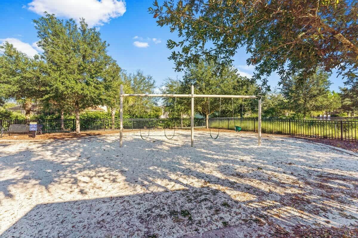 A playground with swings and a fenced area, surrounded by trees and a bench.