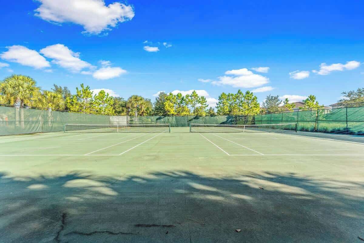 An outdoor tennis court with a net, surrounded by trees and a clear sky.