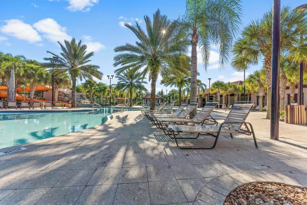 A pool area with lounge chairs, palm trees, and a water slide.