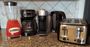 En køkkenbordplade med en rød blender, en sort kaffemaskine, en sølvfarvet espressomaskine og en sølvfarvet brødrister.