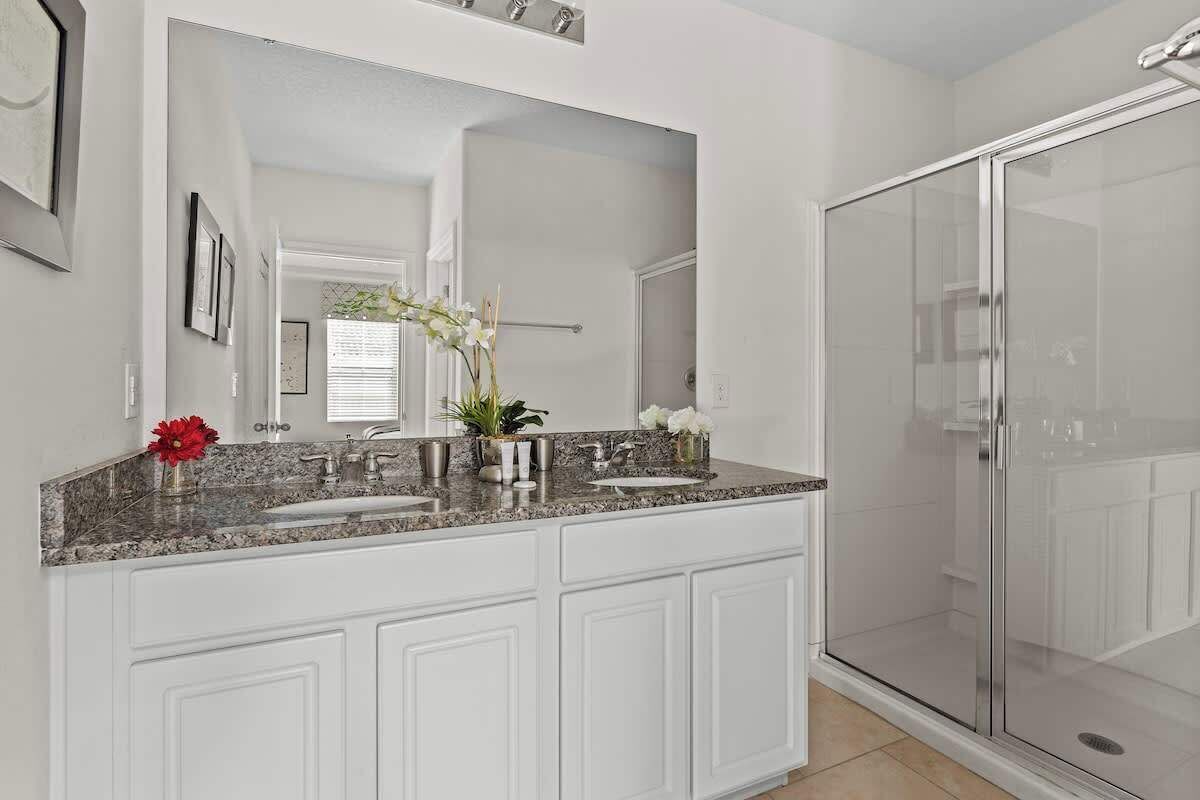 A modern bathroom with a large mirror, a granite countertop, and a walk-in shower.