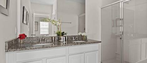A modern bathroom with a large mirror, a granite countertop, and a walk-in shower.