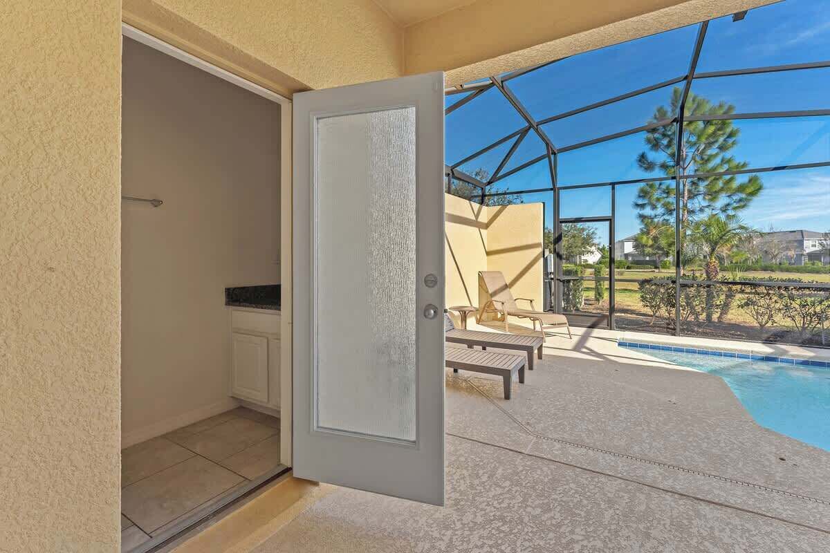An open door leading to a pool area with a view of the outdoors, including a patio with chairs and a pool.