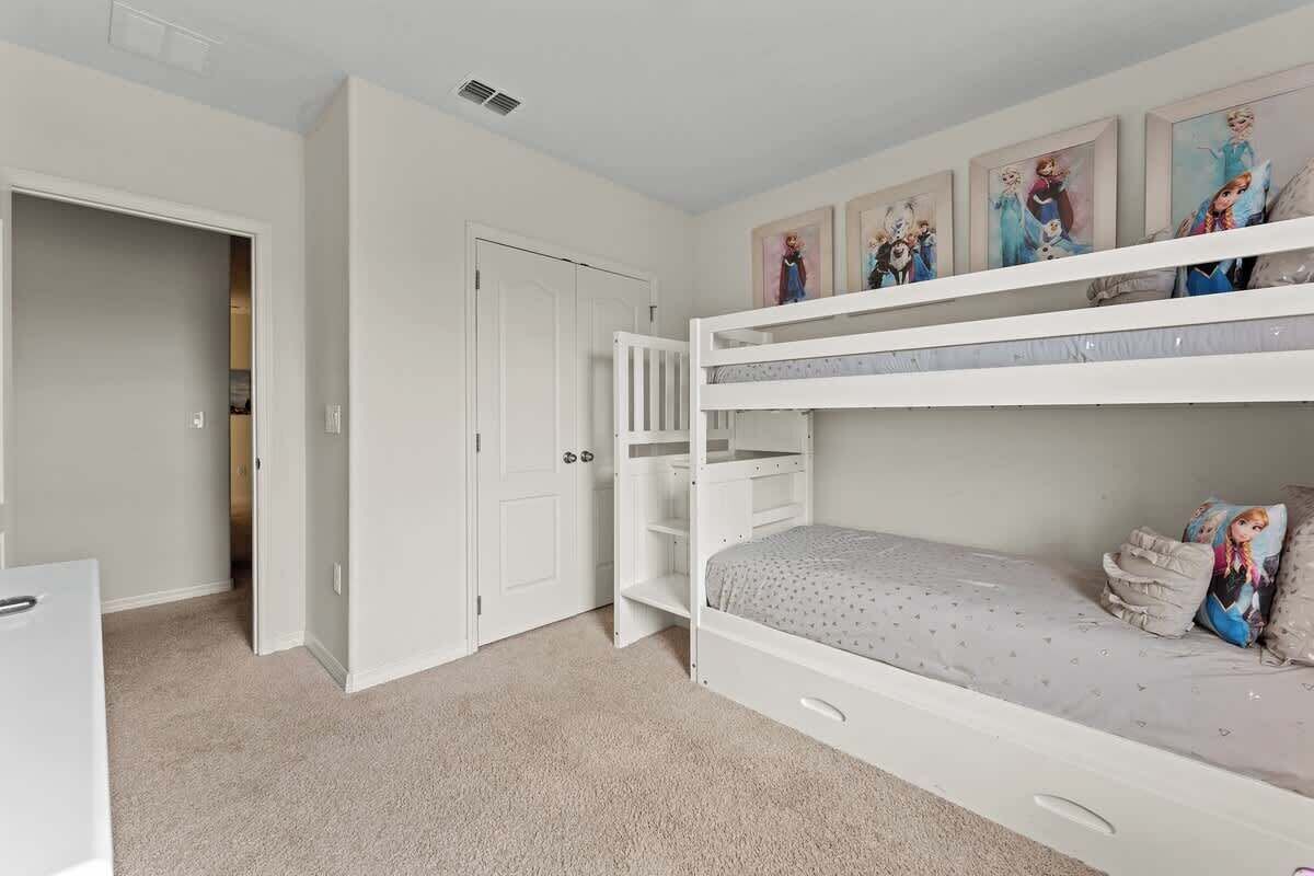 Habitación con literas, una puerta, un armario blanco y una estantería con fotografías enmarcadas.
