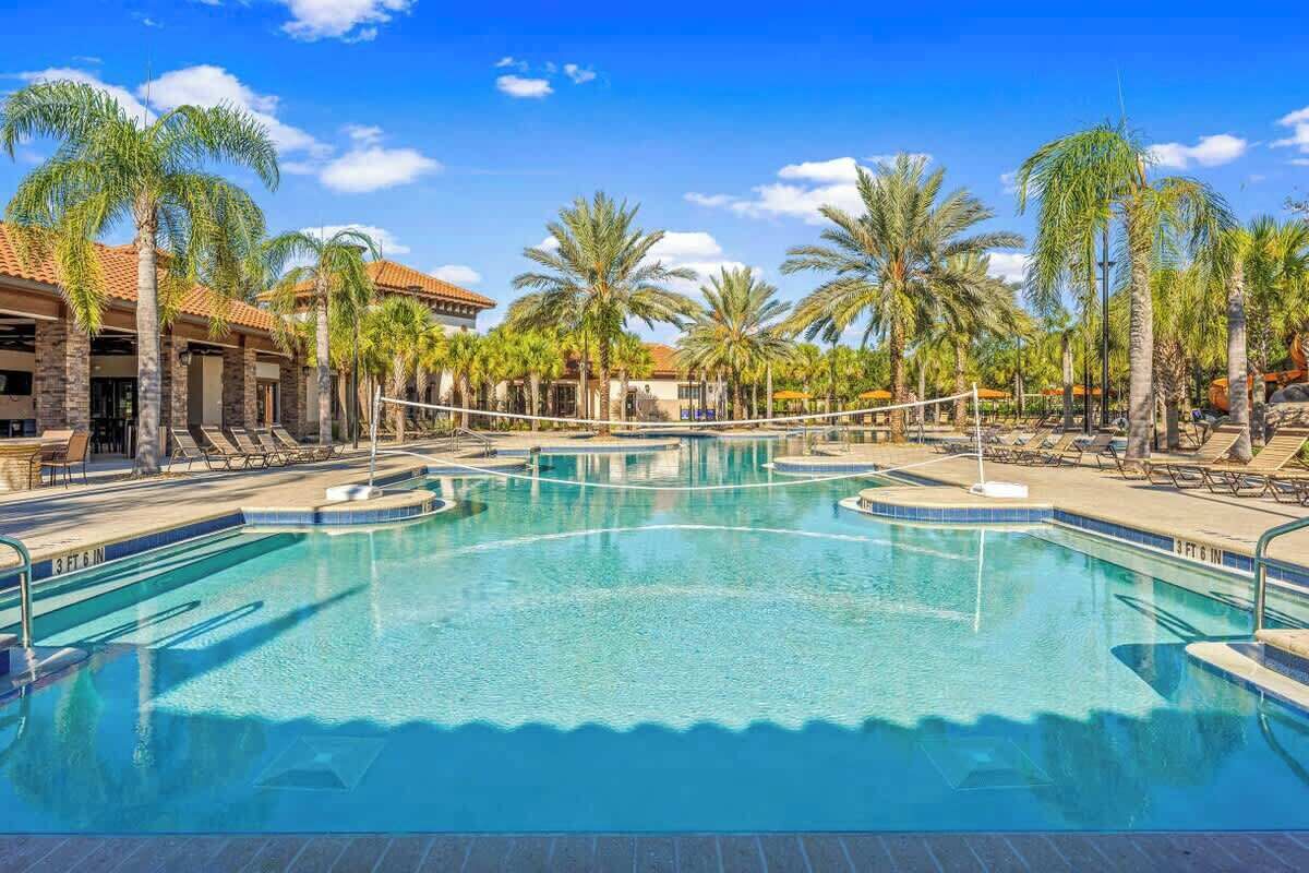 Une piscine avec un filet de volley-ball, entourée de palmiers et de chaises longues.