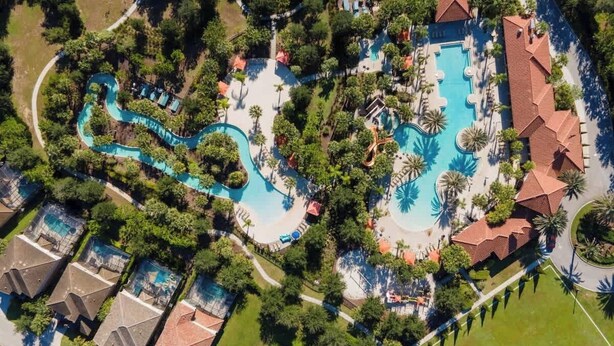 An aerial view of a resort with multiple swimming pools, a winding water slide, and lush landscaping. - Private Pool at Solterra 4BR Townhome (Davenport)