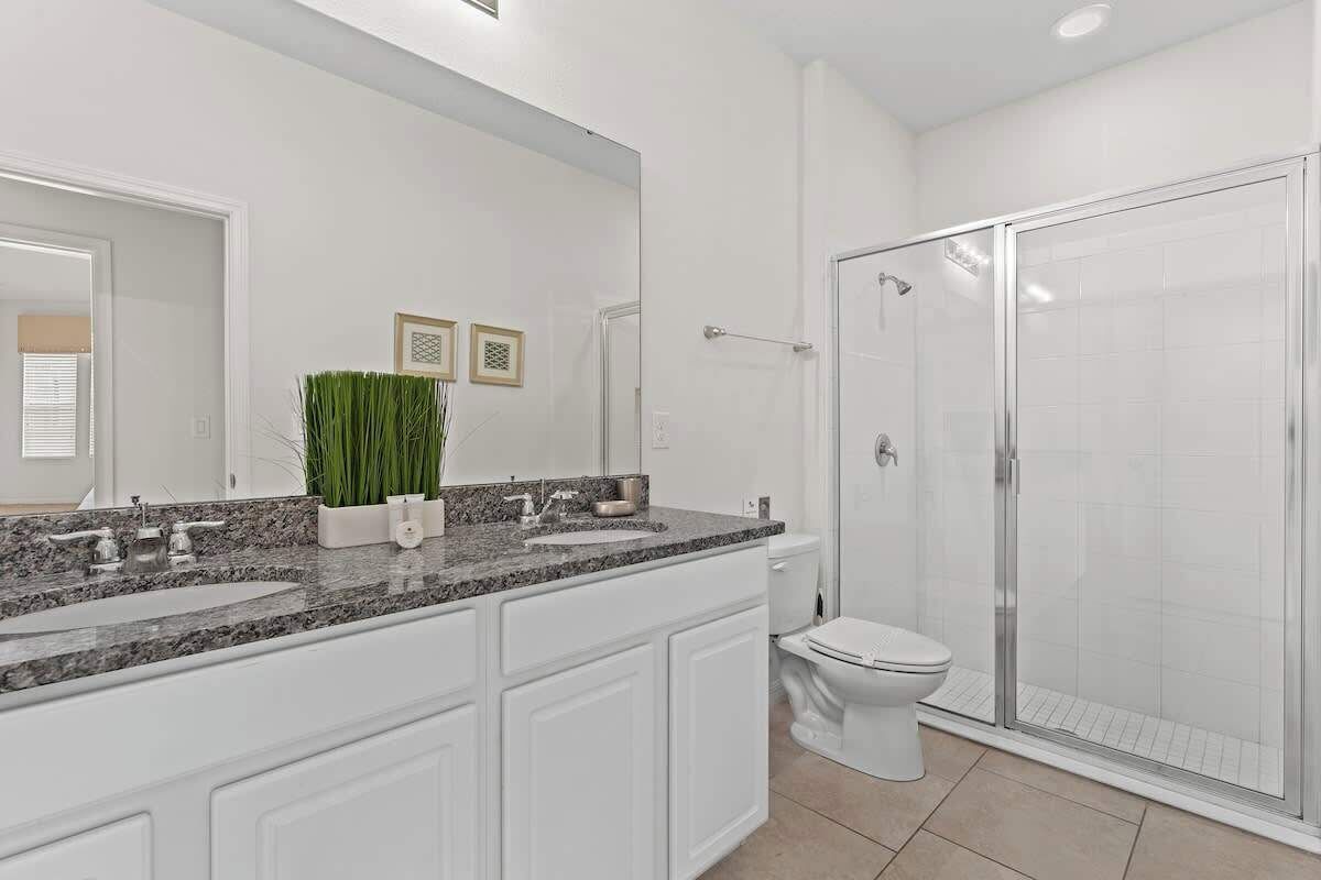 Un bagno moderno con un grande specchio, due lavandini, un water e una cabina doccia in vetro.