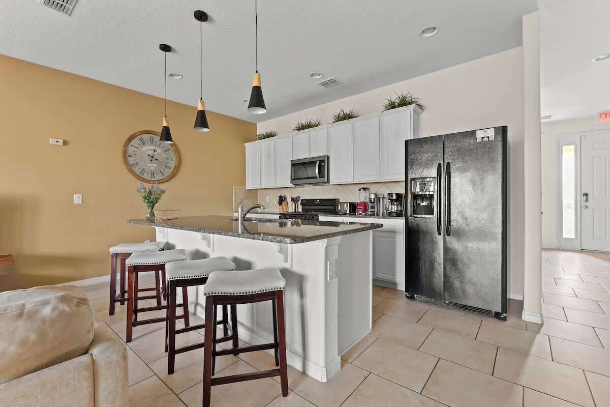 Una cocina moderna con armarios blancos, una isla central con taburetes, un refrigerador grande e iluminación colgante.