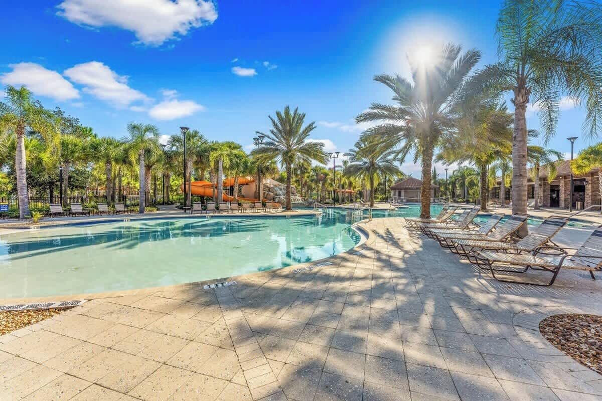 A swimming pool with lounge chairs and palm trees.