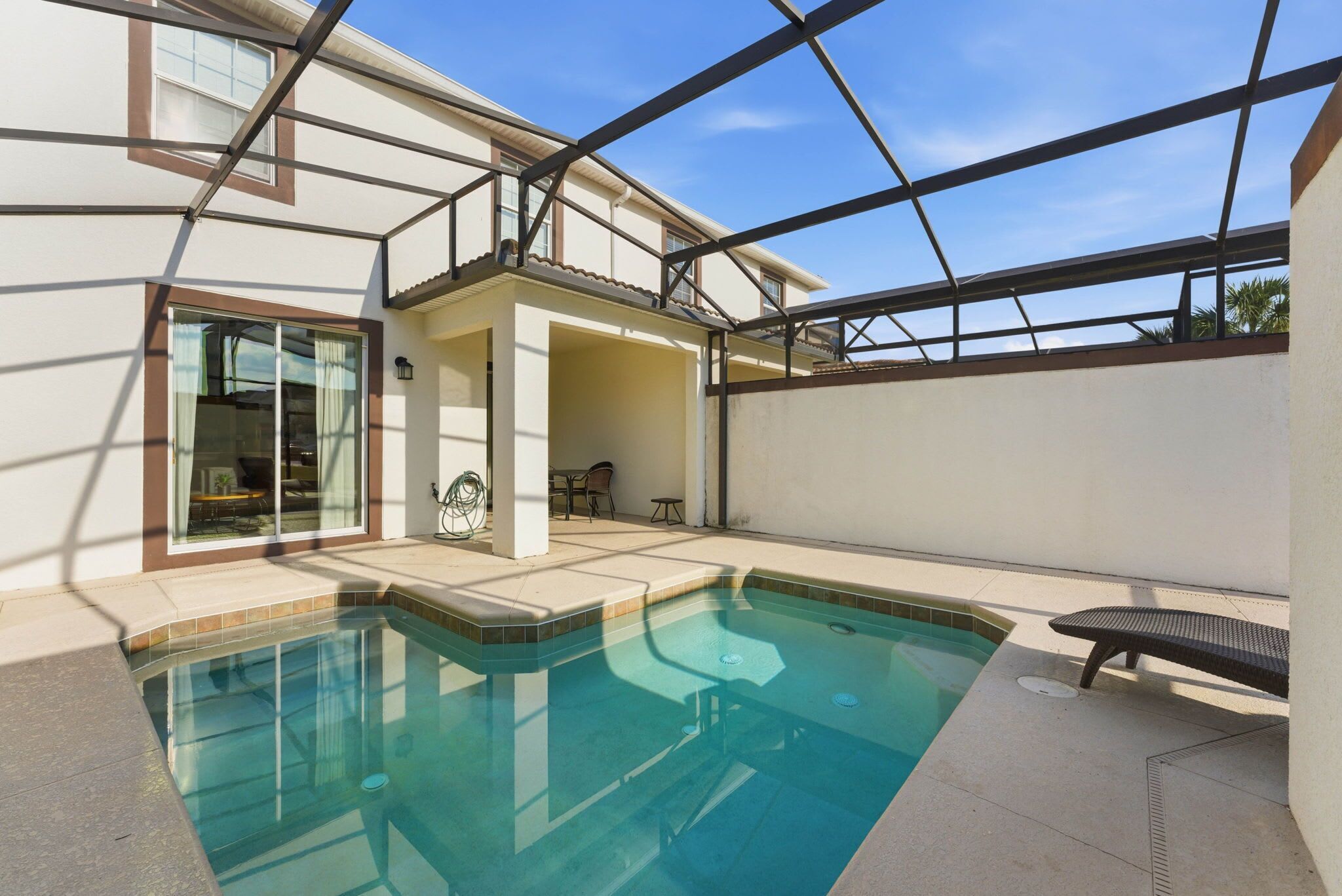 A swimming pool with a clear blue water, surrounded by a covered patio area with a bench.