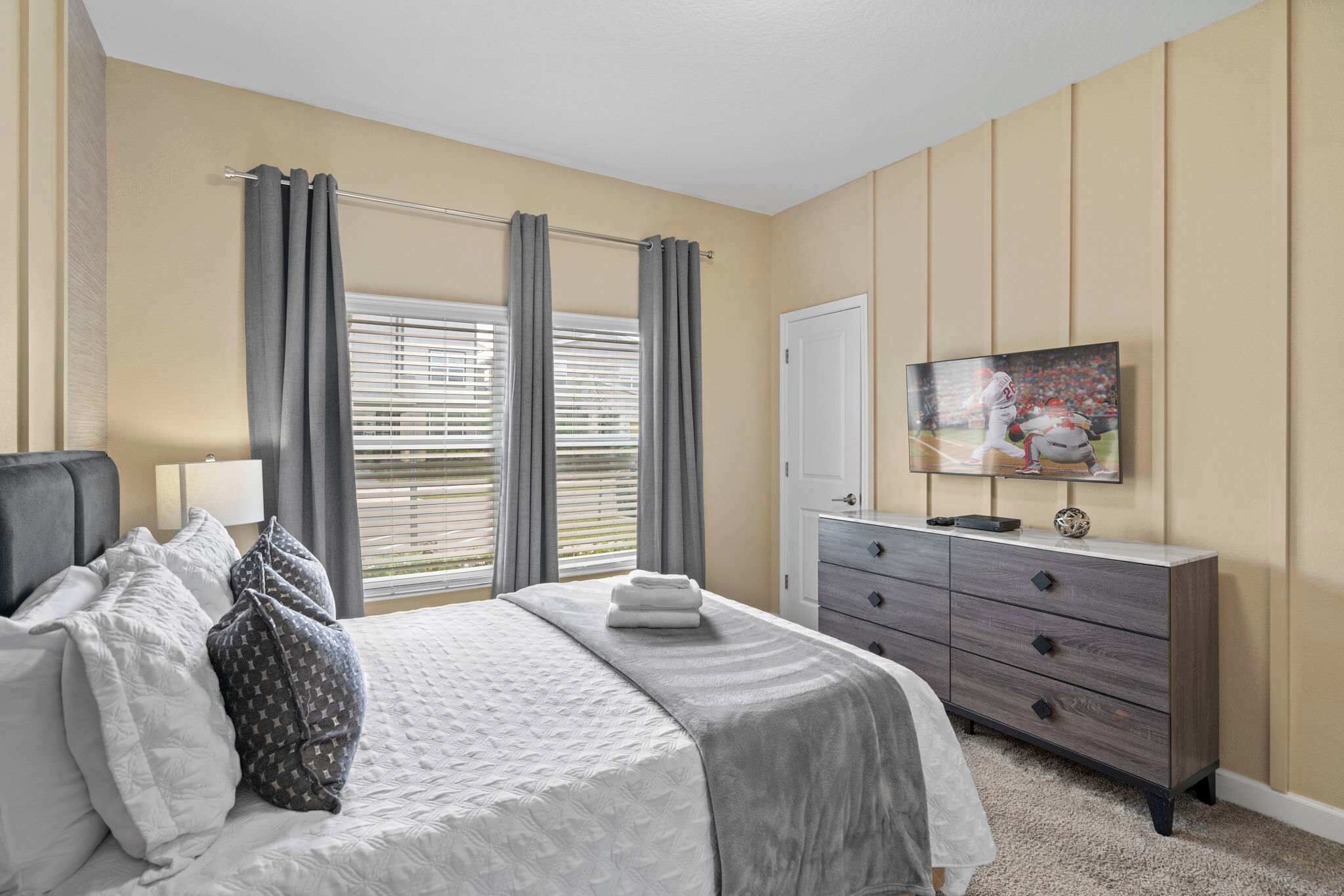 Un dormitorio con cama, cómoda, televisor y ventana con cortinas.